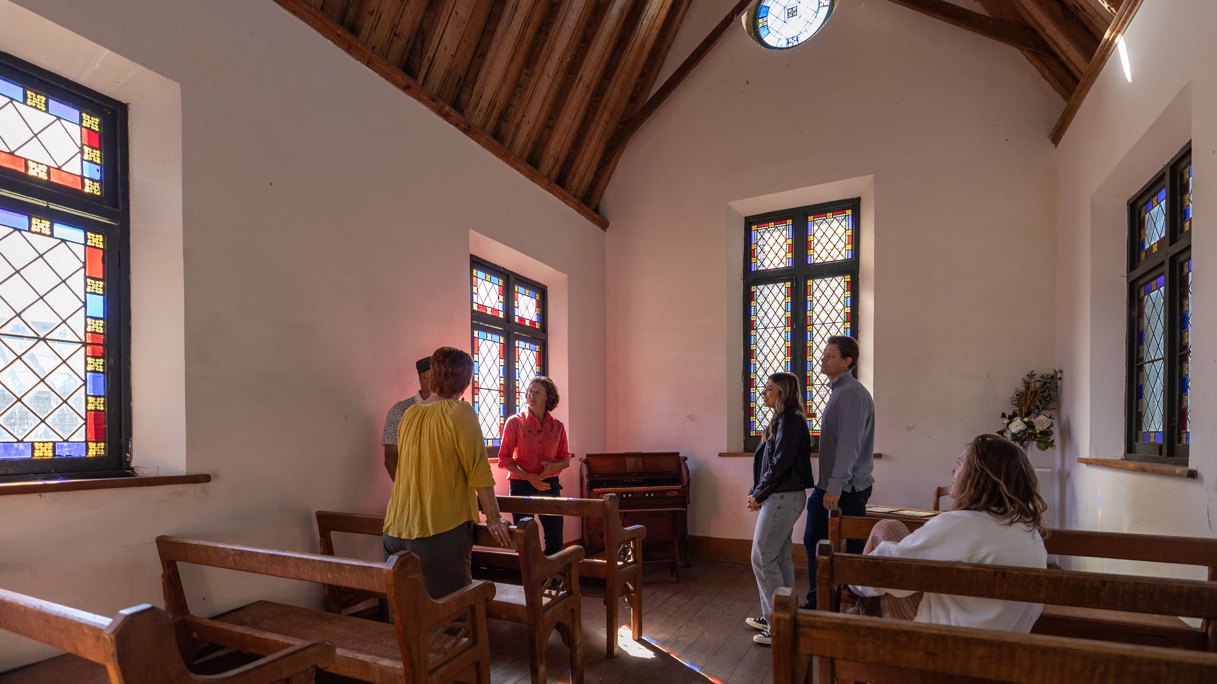 A family group is gathered inside the Chapel and is being guided by a member of the Archer family, learning about the history of the Brickendon Chapel. The Chapel has Huon pine timber pews, stained glass windows and a high pitched timber ceiling and with a circular window high on the end wall. A circa 1900 pedal organ stands in the corner. Photo: Kate von Stieglitz / Tourism Australia.