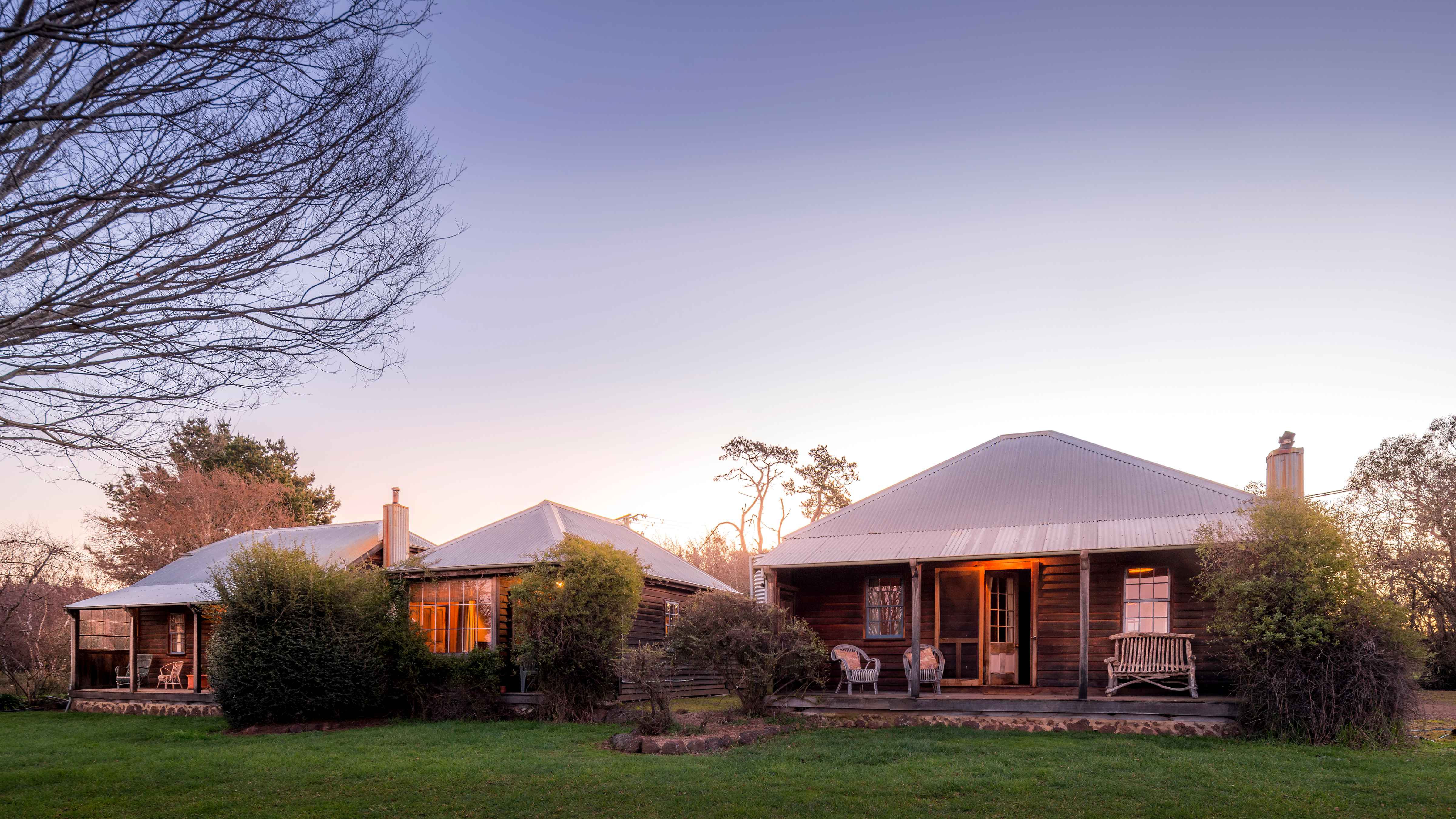 The row of three Farm Cottages constructed in 1986 from recycled materials. They feature timber weatherboards, corrugated iron roofs and Georgian paned windows. Rustic outdoor furniture sits on the verandahs of two of the cottages. Photo: Rob Burnett.