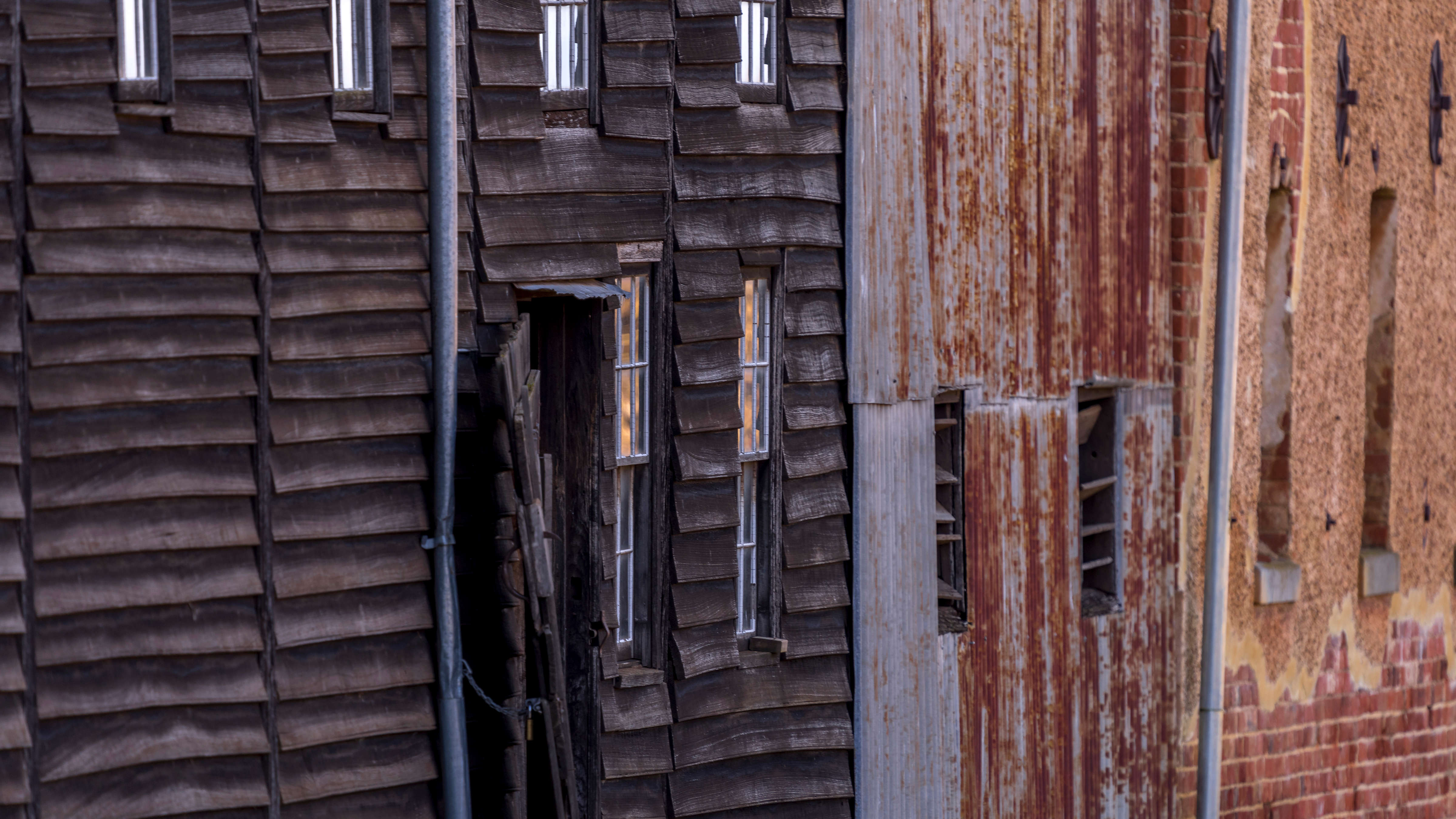 Exterior wall of the shearing shed made up of three materials. The first part is timber weatherboards positioned horizontally with 6 windows and a door set into it. The next part is vertical rust corrugated iron with two windows and the last part in rendered red brick with two more windows. Photo: Rob Burnett.